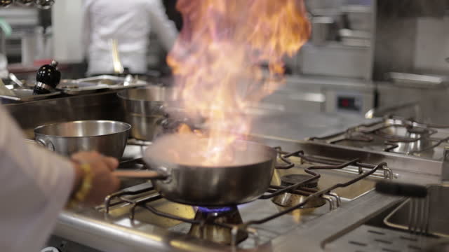 Chef cooking flambe in a pan looking focused,Professional chef cook flambe style, Chef frying mixing food on gas hob in commercial kitchen ,Slow Motion Flambe in Pan of Oil in Commercial Kitchen,Professional chef flambéing in a pan on a gas-fired stove