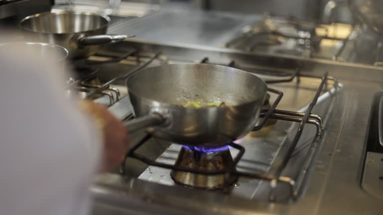 Close-up of chef hand cooking food in frying pan over the gas stove,Professional chef stirs meat in a pan while cooking in a commercial kitchen at a diner,Team of cooking staff preparing a meal working in line,Chef cooking meat at professional kitchen