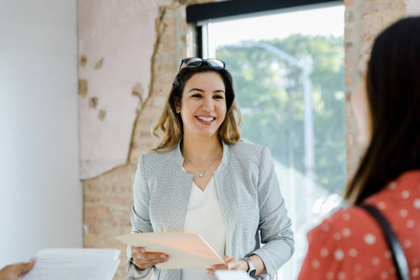 Mid adult female Real Estate Agent smiles at unrecognizable female client The mid adult female real estate agent smiles at the unrecognizable female customer. independence document agreement contract stock pictures, royalty-free photos & images