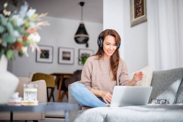 istock Beautiful woman at home sitting on the sofa while using laptop and headphone 1445483752