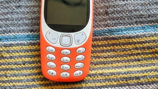 A keypad phone with buttons isolated on black background. Old Cell phone with black display. Closeup of a 2g, 3g orange mobile in India. Technology and social concept.