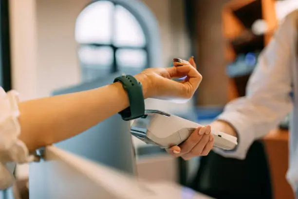 Female using a green smart watch, paying over him, putting it close to the paying machine.