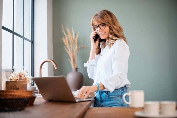 istock Caucasian woman using laptop and cellphon in kitchen 1445489380