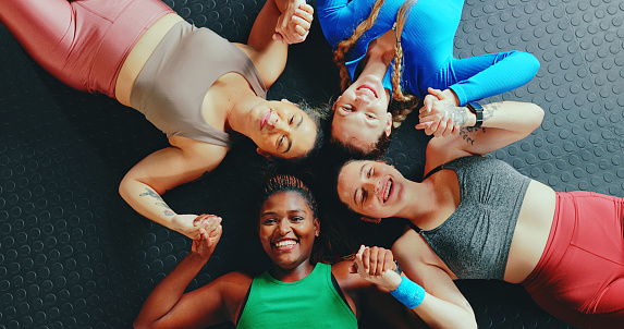 Gym floor, women group support and hold hands together for team fitness exercise, female athlete rest on ground and break from workout class. Top view, diversity and wellness training collaboration