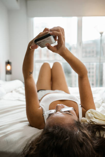 Young mixed race woman using mobile phone  in her bedroom stock photo