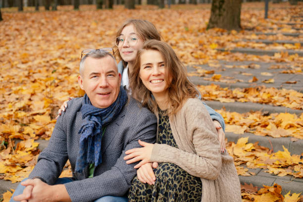 portrait de famille s’embrassant, assise sur des escaliers en béton recouverts de feuilles mortes jaunes parmi les arbres de la forêt du parc. - leaving business landscape men photos et images de collection