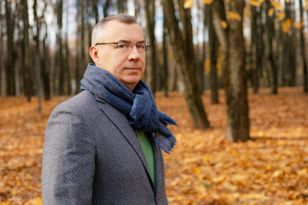 portrait d’un homme d’âge moyen confiant debout près des arbres parmi les feuilles jaunes dans la forêt en automne, regardant la caméra. - leaving business landscape men photos et images de collection