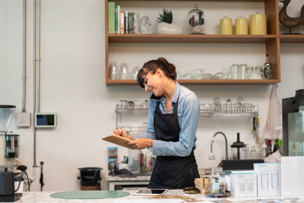 istock Smiling SME female coffee shop owner wearing apron using digital tablet checking and receiving customer order at counter bar. happy successful woman running business. copy space 1445501960