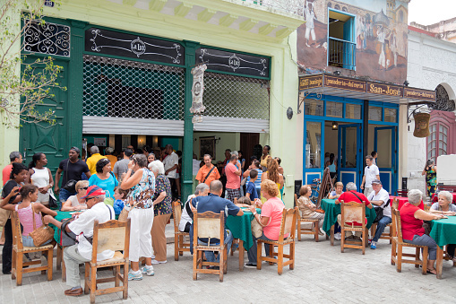 Havana, Сuba - April 10, 2018: People enjoying lunch break at street restaurant, Old Town, Havana, Cuba. Buildings in traditional colonial style are visible in the background.