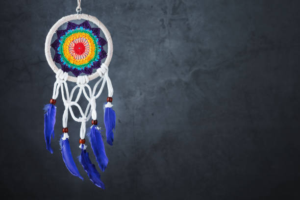 Iron mandala with the Om symbol in the middle, embellished with small bells and spiritual motifs, dangles from a tree branch. The vibrant sunrise paints the sky in rich hues, creating a tranquil and harmonious atmosphere. Color editing. Part of a series.