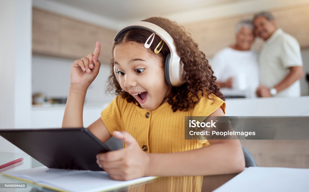 Excited, homeschool tablet or girl with ideas, learning motivation or education innovation in homework study on headphones. Smile, happy and student child with technology in senior grandparents house Child Stock Photo