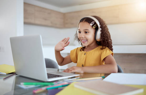 istock Education, laptop and girl learning a virtual class from her kindergarten teacher via an educational online website. Video call, homeschooling and happy student in headphones waving at tutor teaching 1445504511