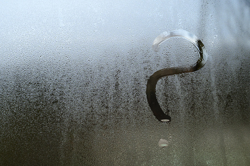 A question mark is drawn on glass with condensation, the effect of fogged windows and glass, an inscription on the glass.