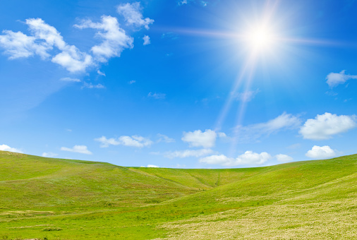 Vast grassy meadow with distant hills, trees and sun.