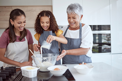 Cooking, girl or women bond helping with milk in dessert, breakfast food or sweet recipe in house or family home kitchen. Happy, smile or baking parent, senior grandmother or learning Brazilian child