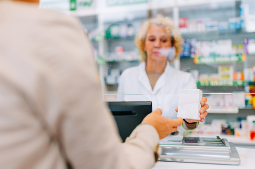 A close up shot of the hands of a pharmacist handing medication over the counter to a customer.