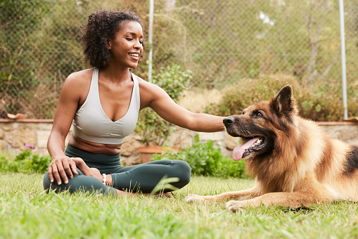 African-American yoga instructor is sitting in the yard petting her beautiful dog. Copy space