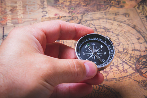 Adventure search. Compass and maps. Treasure hunt on island. Pirate map. Person holds compass in his hand.