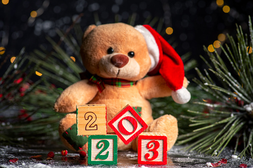 2023 New Year festive background with wooden numbers showing the upcoming year and Christmas symbol soft toy. New Year background with Christmas festive lights and symbols. White painted wood created the inscription Number 2023 on a dark background