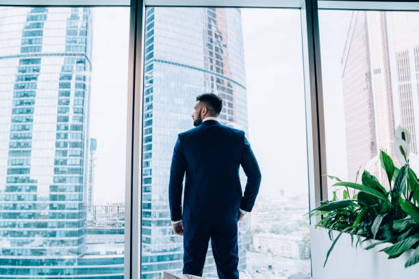 istock Serious smart businessman standing at window in office 1445520180