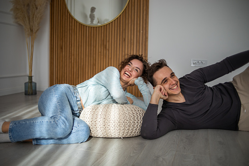A nice attractive Caucasian couple is lying on the floor, enjoying a nice morning in their new apartment, they have just moved into a new apartment, they are dressed casually.