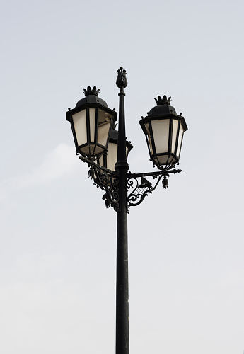 Typical street lamps in a historic Algarve town in Portugal. View from below against a pale blue sky.
