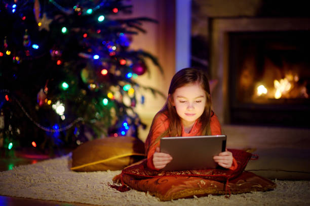 Adorable little girl using a tablet pc by a fireplace on Christmas evening stock photo