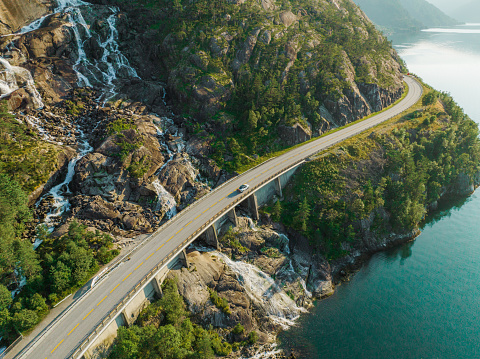 Scenic aerial view of  car on the road near waterfall that falls into fjord in Norway