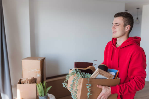 Student smiling when looking through the college dorm window with a box in his hands stock photo