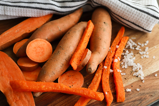 Raw sweet potato cut into halves, discs and fries with salt granules in the background