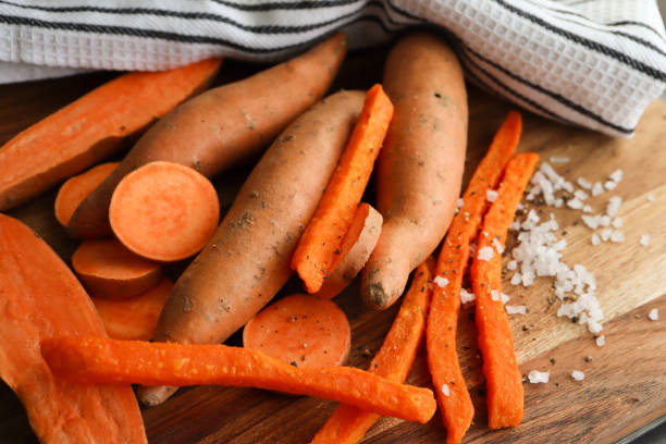 Sweet potatoes Raw sweet potato cut into halves, discs and fries with salt granules in the background carotene stock pictures, royalty-free photos & images