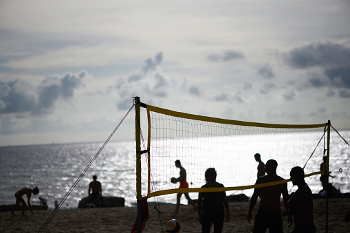 Silhouette of unrecognizable people playing beach volleyball at sunset, copy space