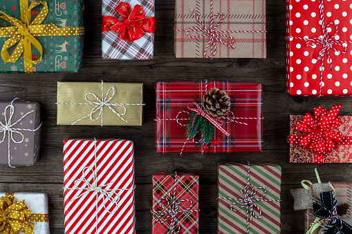 Christmas background of beautifully wrapped gift boxes of various shapes and sizes with tied bows on wooden rustic table. Flat lay.