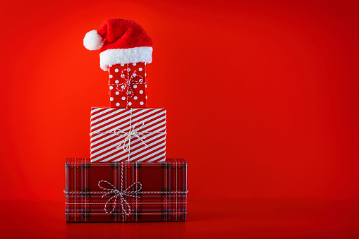 Christmas red background with Christmas presents. Christmas concept. Beautifully wrapped gift boxes in the shape of Christmas tree with Santa hat on the top on red background.