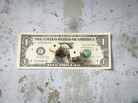 The dollars value is a roll of the dice, a concept of cash value. Snake eyes roll up on an American dollar bill, on a concrete background with copy space.