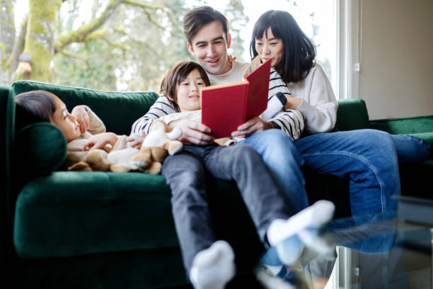 istock Family Relaxes At Home Together on Sofa With Book 1445556959