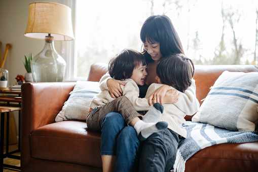 A Japanese mom hugs her two children as they relax on the couch at home.  Loving and supportive parent.