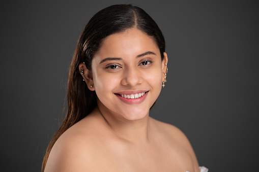 Headshot of smiling pretty latino girl on grey studio background