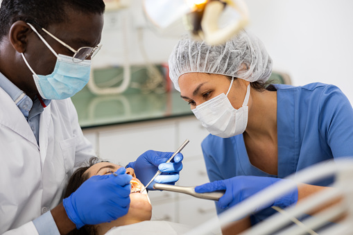 Focused african american stomatologist with female assistant treating teeth to woman patient in modern dental office