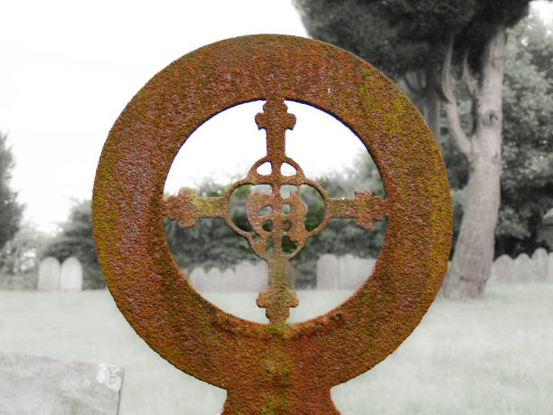 Rusty old iron circle with ornate cross headstone in England.