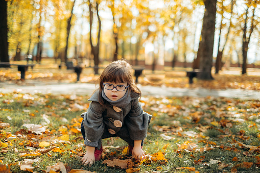Happy cute girl in a fashionable coat and stylish glasses walks and laughs, the child enjoys time in a warm autumn park, a happy childhood