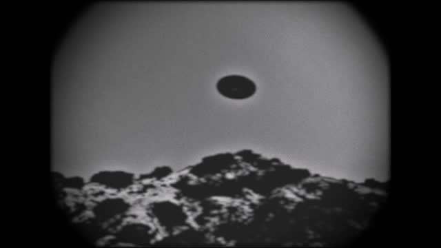 Kine scope looking footage of a UFO flying over a mountain.