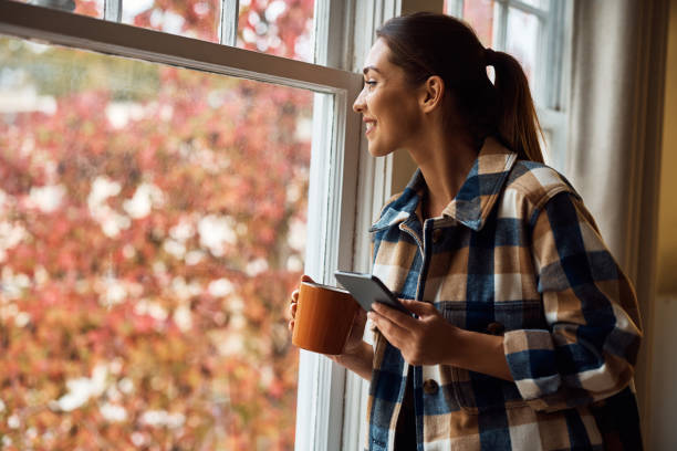 istock Happy woman using mobile phone while looking out the window. 1445574913