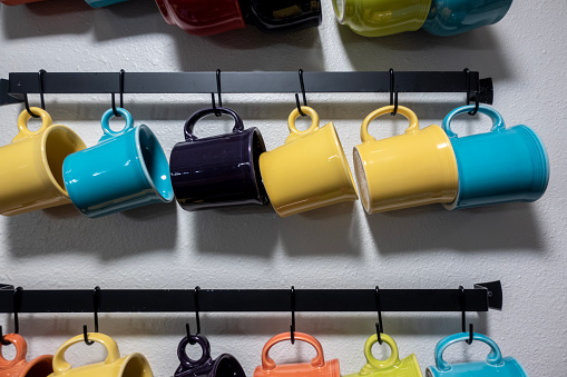 A collection of colorful mugs hanging on black hooks against a white wall
