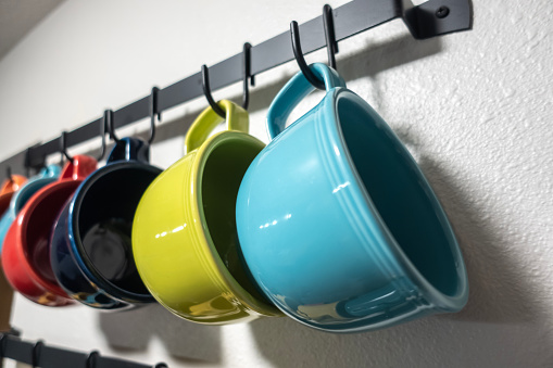 A collection of colorful mugs hanging on black hooks against a white wall