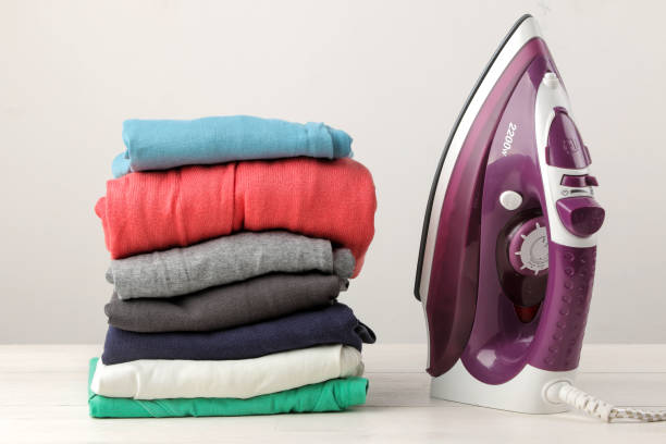 istock lilac iron and a stack of clothes on a light background. ironing clothes. household electrical appliances. 1445579601