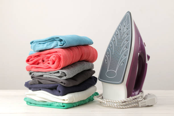 istock lilac iron and a stack of clothes on a light background. ironing clothes. household electrical appliances. 1445579602