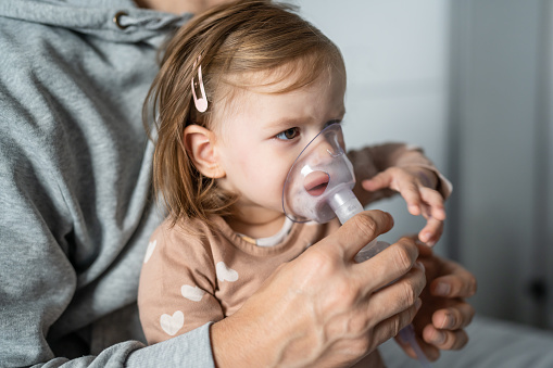 one toddler using nebulizer at home small girl child using vapor steam inhaler mask inhalation at home medical procedure medicament treatment asthma pneumonia bronchitis selective focus
