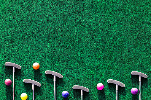 Multiple mini golf clubs and balls on putting green background