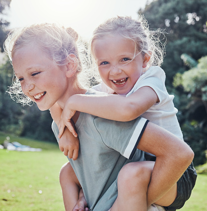 Happy, smile and siblings in an outdoor park during summer having fun and playing in nature. Happiness, excited and girl children on an adventure giving a piggy back ride outside in a green garden.